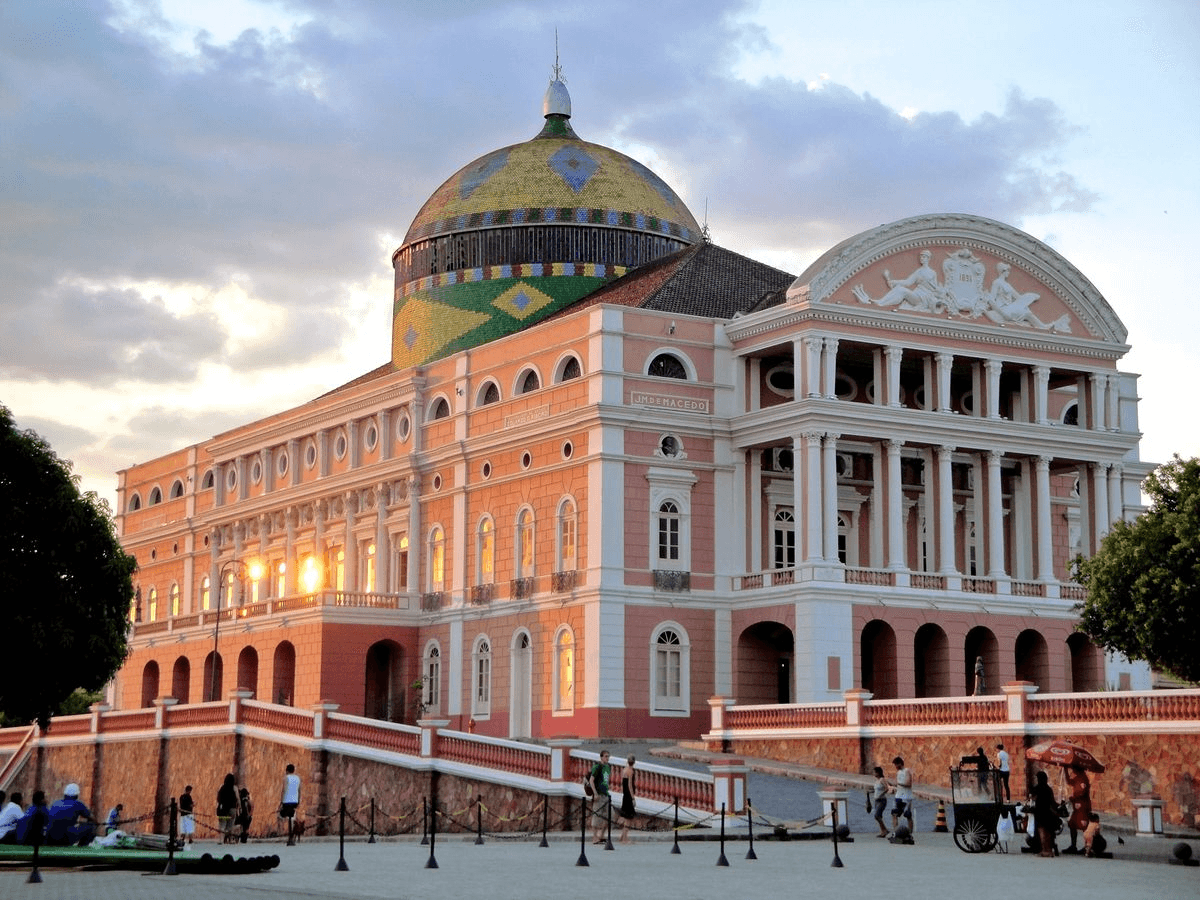 Teatro Amazonas ao entardecer, com sua cúpula colorida e a fachada rosa iluminada pelo sol